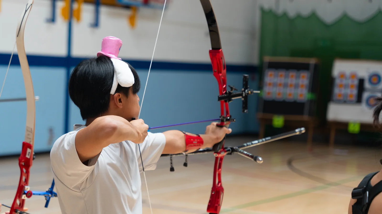 An archer at full draw during an ISAA indoor intervarsity, with targets in the background